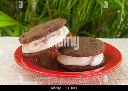 Glace à la fraise en sandwich entre deux biscuits au chocolat sur une plaque rouge à l'extérieur Banque D'Images