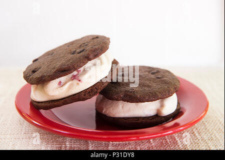 Ice Cream Sandwich à la crème glacée aux fraises entre deux biscuits au chocolat sur une plaque rouge Banque D'Images