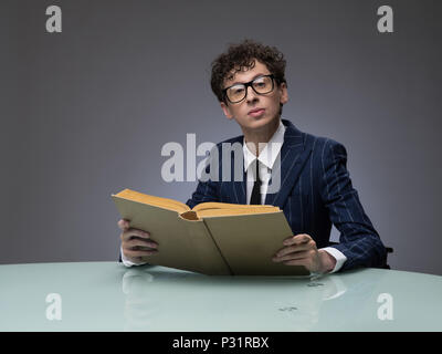 L'homme drôle en costume rayé la lecture d'un livre sur fond gris. Acteur professionnel de l'expression du visage. Banque D'Images
