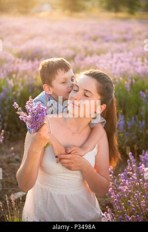 Cute little boy kissing son doucement belle jeune mère en été champ bloom Banque D'Images