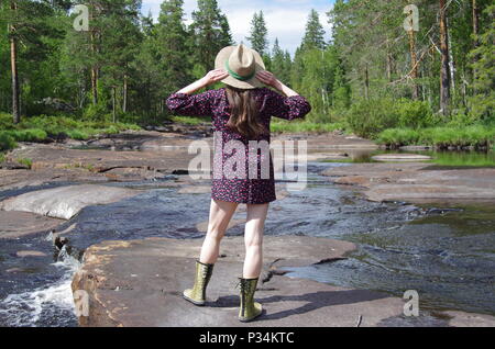 Belle jeune femme avec une robe courte et un chapeau est profitant de la chaude journée d'été à proximité d'une rivière dans la forêt Banque D'Images