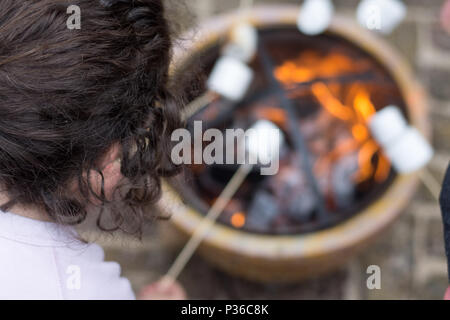 Girl toasting mash mallows sur open fire pit at garden party Banque D'Images