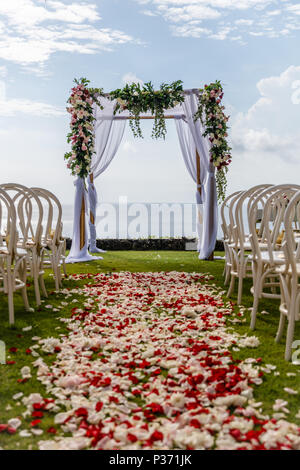 Arche de mariage près de l'océan pour une cérémonie décorée de tissu blanc et des fleurs fraîches, des chaises et des pétales de rose blanche et rouge allée. Bali, Indonésie. Banque D'Images