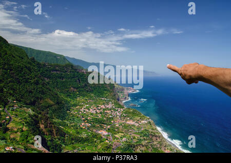 Main de l'homme pointant sur la côte nord de l'île de Madère, Santana ville entourée par de hautes montagnes et d'un bleu profond de l'océan Atlantique. Popula Banque D'Images