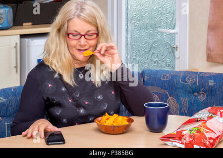 Blonde woman eating Doritos à partir d'un sac de taille de partage et un petit bol Banque D'Images