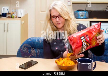 Blonde woman eating Doritos à partir d'un sac de taille de partage et un petit bol Banque D'Images