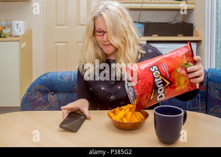 Blonde woman eating Doritos à partir d'un sac de taille de partage et un petit bol Banque D'Images