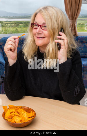 Blonde woman eating Doritos à partir d'un sac de taille de partage et un petit bol Banque D'Images