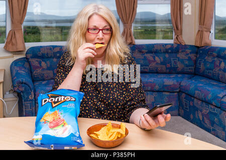 Blonde woman eating Doritos à partir d'un sac de taille de partage et un petit bol Banque D'Images