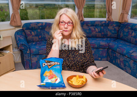 Blonde woman eating Doritos à partir d'un sac de taille de partage et un petit bol Banque D'Images