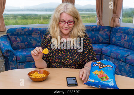 Blonde woman eating Doritos à partir d'un sac de taille de partage et un petit bol Banque D'Images