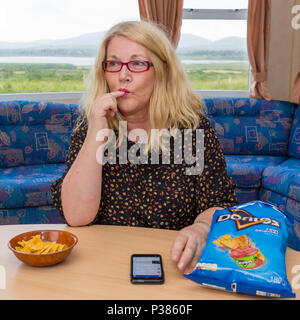 Blonde woman eating Doritos à partir d'un sac de taille de partage et un petit bol Banque D'Images