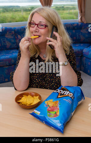 Blonde woman eating Doritos à partir d'un sac de taille de partage et un petit bol Banque D'Images