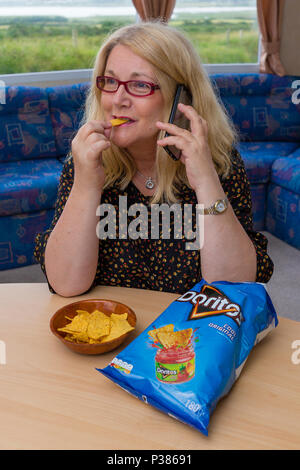 Blonde woman eating Doritos à partir d'un sac de taille de partage et un petit bol Banque D'Images