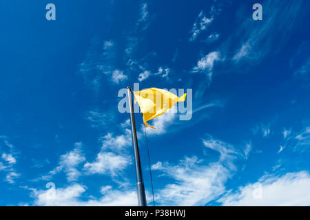 Drapeau jaune sur un poteau, voletant dans la brise contre un ciel bleu à Kota Kinabalu, Bornéo Banque D'Images