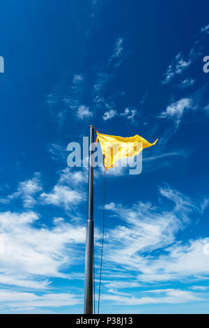 Drapeau jaune sur un poteau, voletant dans la brise contre un ciel bleu à Kota Kinabalu, Bornéo Banque D'Images