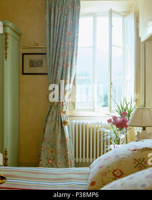 Coussins floraux sur lit dans la campagne toscane à la chambre avec des rideaux vert pâle à la fenêtre Banque D'Images