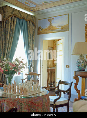 Jeu d'échecs sur table de salle à manger avec un chiffon à motifs en toscan élégant avec de lourdes tentures bleu et crème Banque D'Images