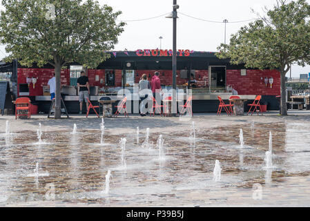 Les gens d'acheter des fruits de mer au copine's seafood stand, le port de Folkestone, Kent, Angleterre, Royaume-Uni. Une caractéristique fontaine jet d'eau au premier plan le pavage. Banque D'Images