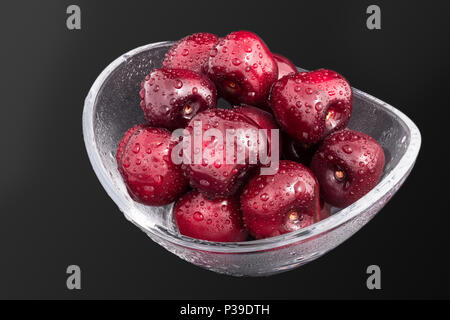 Close-up de laver les cerises dans un bol en verre. Prunus avium. Belle pile de fruits frais dans le plat. Gouttes d'eau. Collation saine juteuse. Fond noir. Banque D'Images