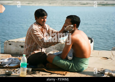 VARANASI, INDE - 10 février : salon de coiffure de la rue un homme de rasage à l'aide d'une lame de rasoir sur une banque du fleuve sacré du Gange à Varanasi . 10 février 2008, Banque D'Images