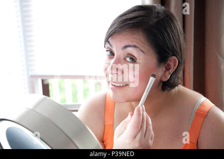 Une belle femme met sur l'ombre d'oeil et vous sourit. Banque D'Images