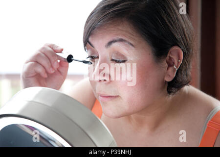 Par une fenêtre, une femme brunnette applique son maquillage des yeux Banque D'Images