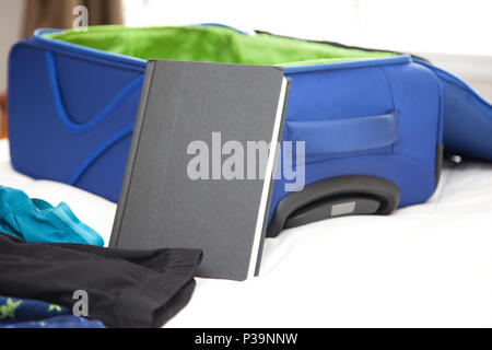 Une couverture rigide livre noir avec copie espace vide à côté d'une valise de voyage Banque D'Images