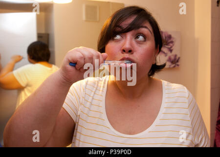 Une femme brosse les dents dans la salle de bains et pose ses yeux dans la pensée Banque D'Images