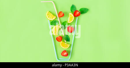 Mise en page créative ingrédients limonade aux fraises - citron, menthe, baies de tomber dans le verre à cocktail avec une paille sur fond vert. Des boissons d'été. Banque D'Images