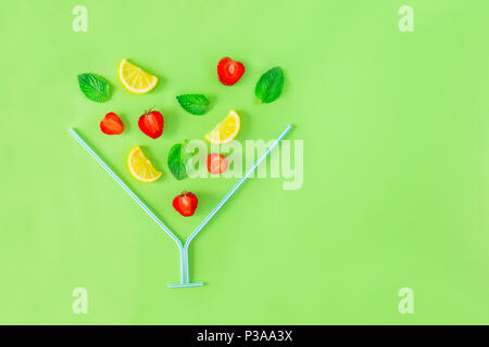 Mise en page créative, ingrédients - citron limonade aux fraises, menthe, baies de tomber dans le verre cocktail fait avec paille sur fond vert. Des boissons d'été. Banque D'Images