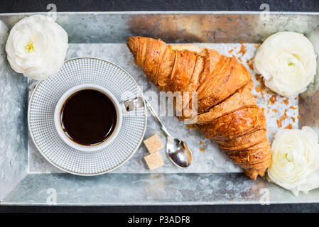 Petit-déjeuner léger de croissants frais et une tasse de café sur le bac gris, Ranunculus fleurs à proximité Banque D'Images