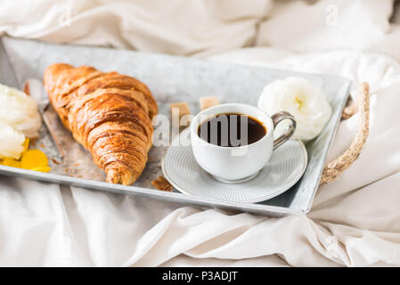 Petit-déjeuner au lit de croissants frais et une tasse de café sur le bac gris, Ranunculus fleurs à proximité Banque D'Images