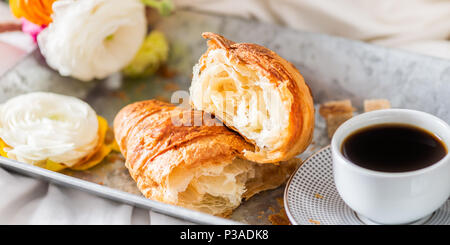 Petit-déjeuner au lit de croissants frais et une tasse de café sur le bac gris, Ranunculus fleurs à proximité Banque D'Images
