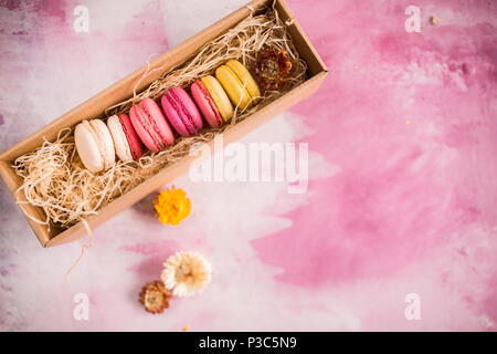 Rangée de macarons gâteau en boîte-cadeau sur fond lumineux. Close up macaron dessert au vue du dessus. Biscuits aux amandes colorées en rose pastel, jaune. V Banque D'Images