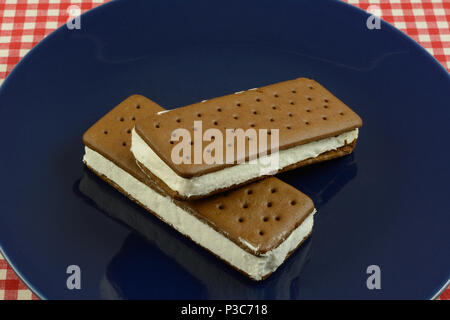 Deux sandwiches à la crème glacée congelés sur plaque bleue sur la nappe à carreaux rouges et blancs Banque D'Images