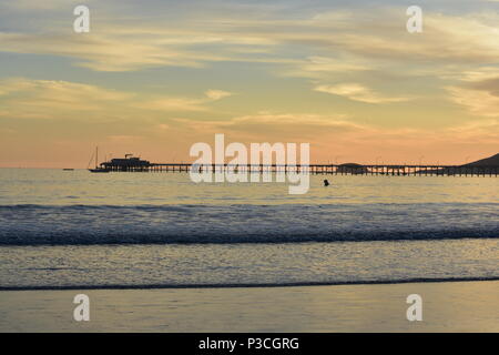 Coucher du soleil et le fracas des vagues doucement avec l'Avila Beach Pier dans l'arrière-plan à Avila Beach, CA. Banque D'Images