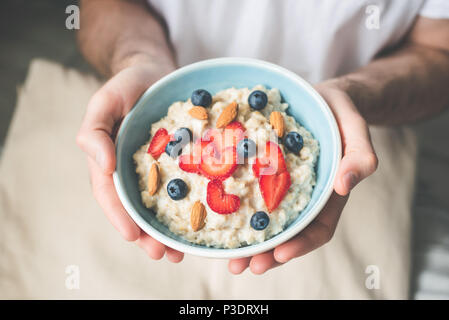 Petit déjeuner porridge d'avoine bol avec des baies et des noix dans les mains. Végétarien, bonne hygiène de vie, alimentation saine, matin concept Banque D'Images