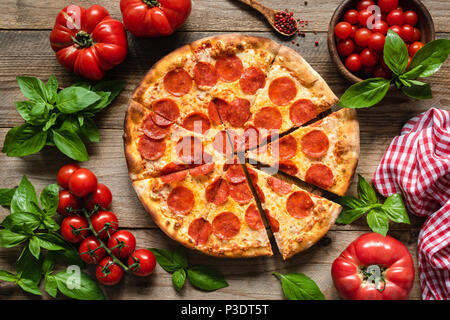 Pizza au pepperoni, tomates et basilic. Pizza au pepperoni savoureux sur fond de bois rustique. Vue de dessus de la pizza italienne Banque D'Images