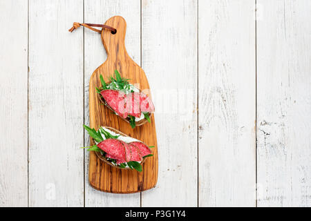 Savoureux hors-d'émincé de salami épicé sur du pain avec du fromage et des herbes sur une planche à découper, copy space Banque D'Images