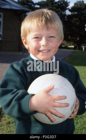 Quatre ans portant un uniforme scolaire holding a football. Banque D'Images