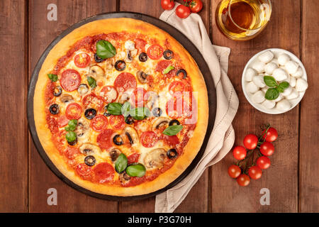 Une photo prise à la verticale de pepperoni pizza avec un verre de vin blanc, tomates cerises et mozzarellini fromage, tourné à partir de ci-dessus, sur un fond rustique foncé Banque D'Images