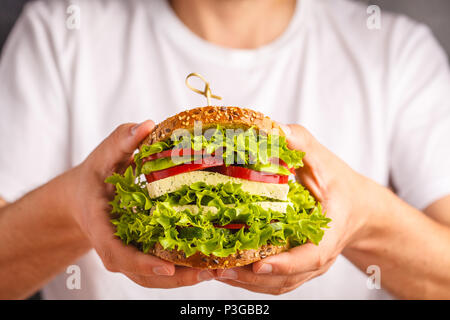 Gros sandwich végétalien au tofu et légumes frais dans les mains des hommes, fond blanc. Banque D'Images