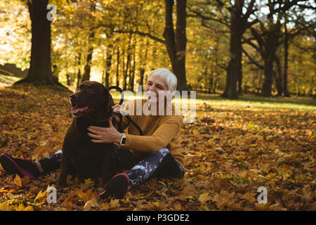 Senior woman sitting on ground et caressant son chien dans le parc Banque D'Images