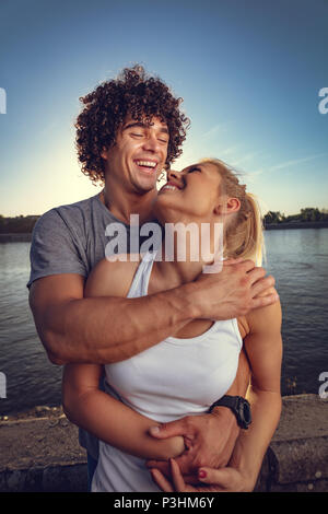 Beau jeune couple hugging et repos après une formation réussie par la rivière au coucher du soleil. Banque D'Images