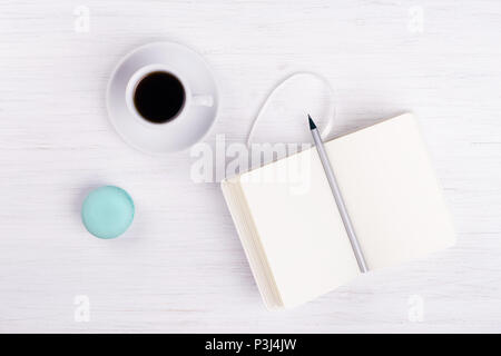 Une tasse de café, macaron, bloc-notes et crayon sur la table en bois blanc. Banque D'Images