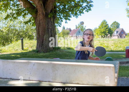 Une fillette de 7 ans joue au tennis de table sur une table de ping-pong. Elle est axée sur frapper la balle avec son bat Banque D'Images