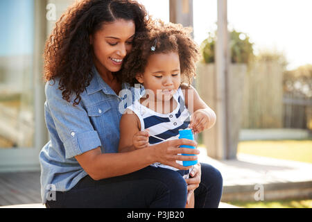 Young mixed race mother and daughter blowing bubbles en dehors Banque D'Images