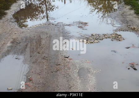 Photo d'un fragment d'une route détruite avec de grandes flaques d'eau par temps de pluie Banque D'Images