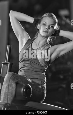 Exercices de force de femme pour les abdominaux à salle de sport salle de sport. Girl doing yoga s'étend après l'exécution. Modèle de remise en forme dans le noir sport club. B Banque D'Images